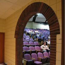 Arched brick doorway leading to a lecture hall with purple seats.